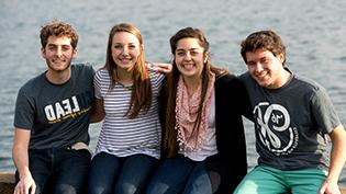 A group of students sit on a brick wall by Cedar Lake