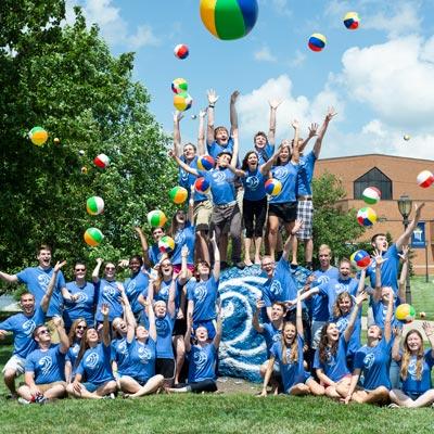 picture of students celebrating on the Cedarville rock while wearing cove shirts and tossing beach balls in the air