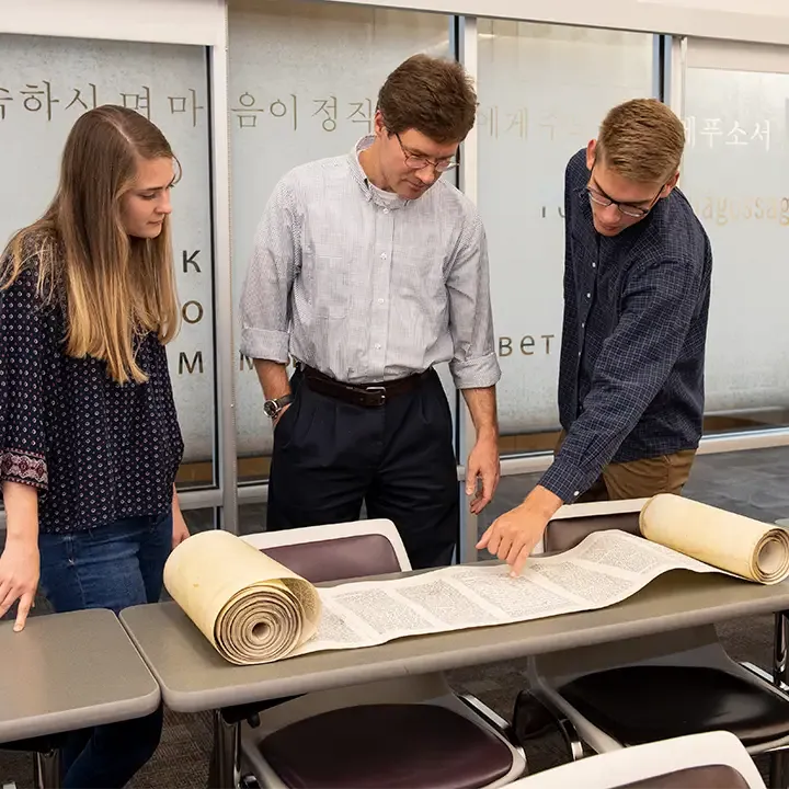 Three people standing over an open scroll